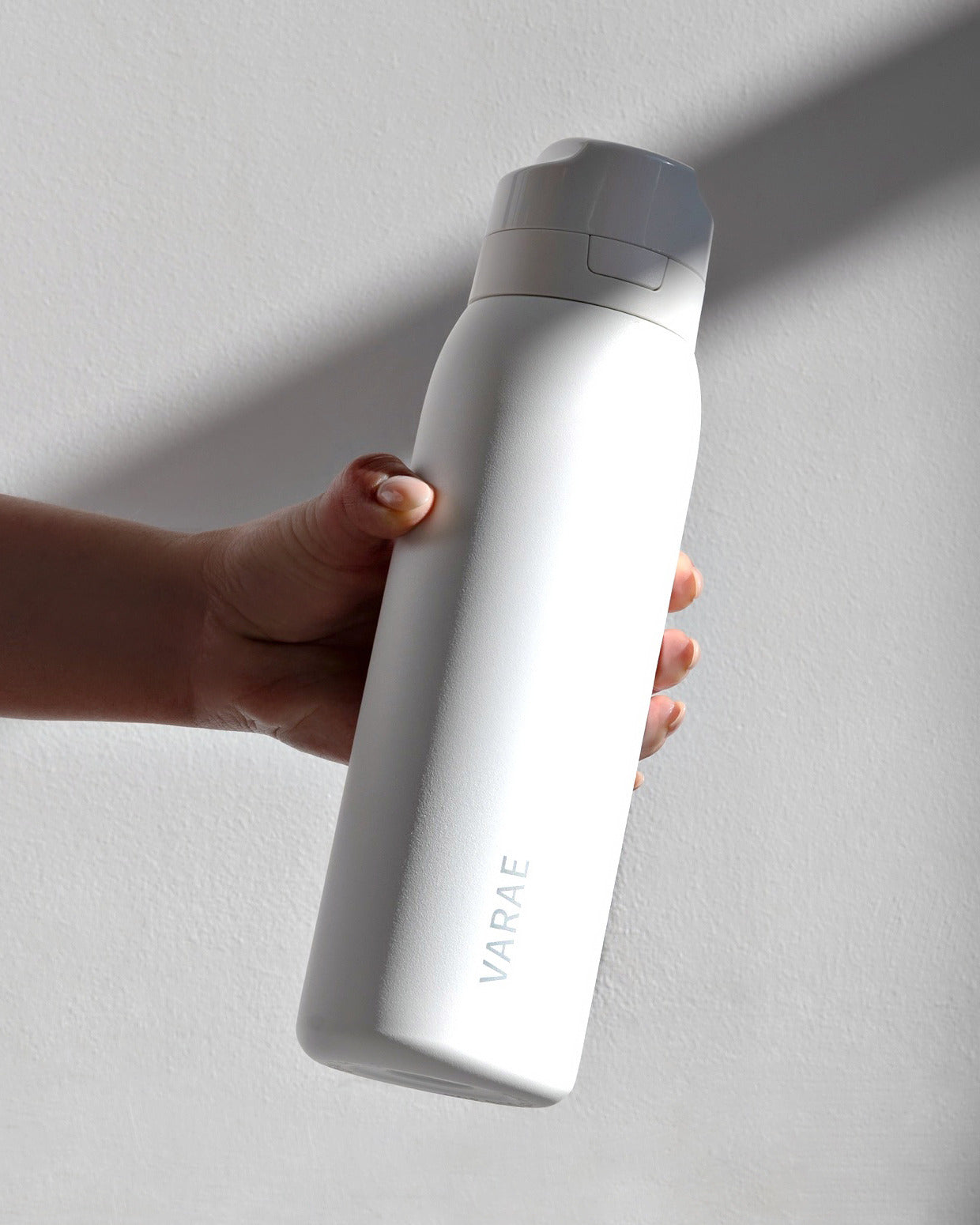 A hand holding the VARAE Pure bottle in window light.