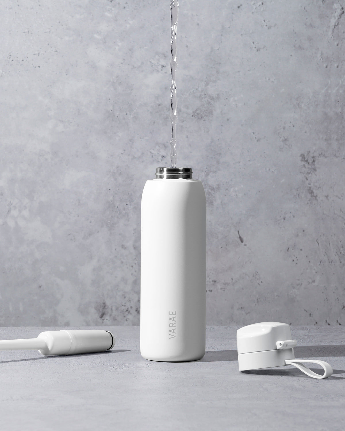 VARAE Pure bottle being filled, with the lid and filter set beside it on a grey stone surface